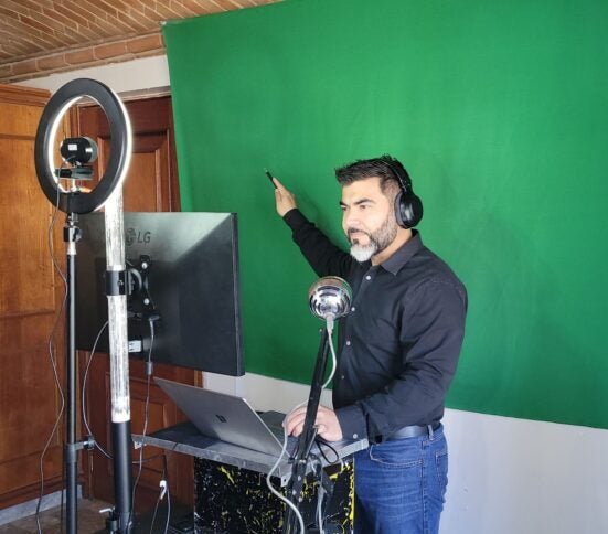 Virtual Educator at a standup workstation with microphone and headphones pointing to the green screen behind him