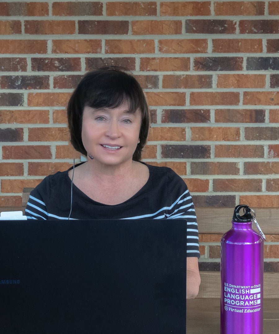 Virtual Educator sitting in front of a brick wall using a laptop with an English Language Programs water bottle placed for hydration