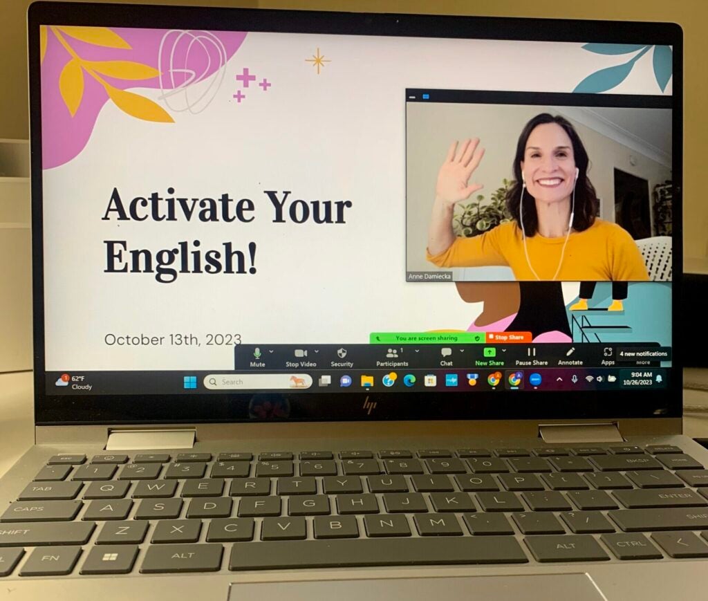 A photo of a laptop on which there is a video still of Anne Damiecka and a slide that reads "Activate Your English!"