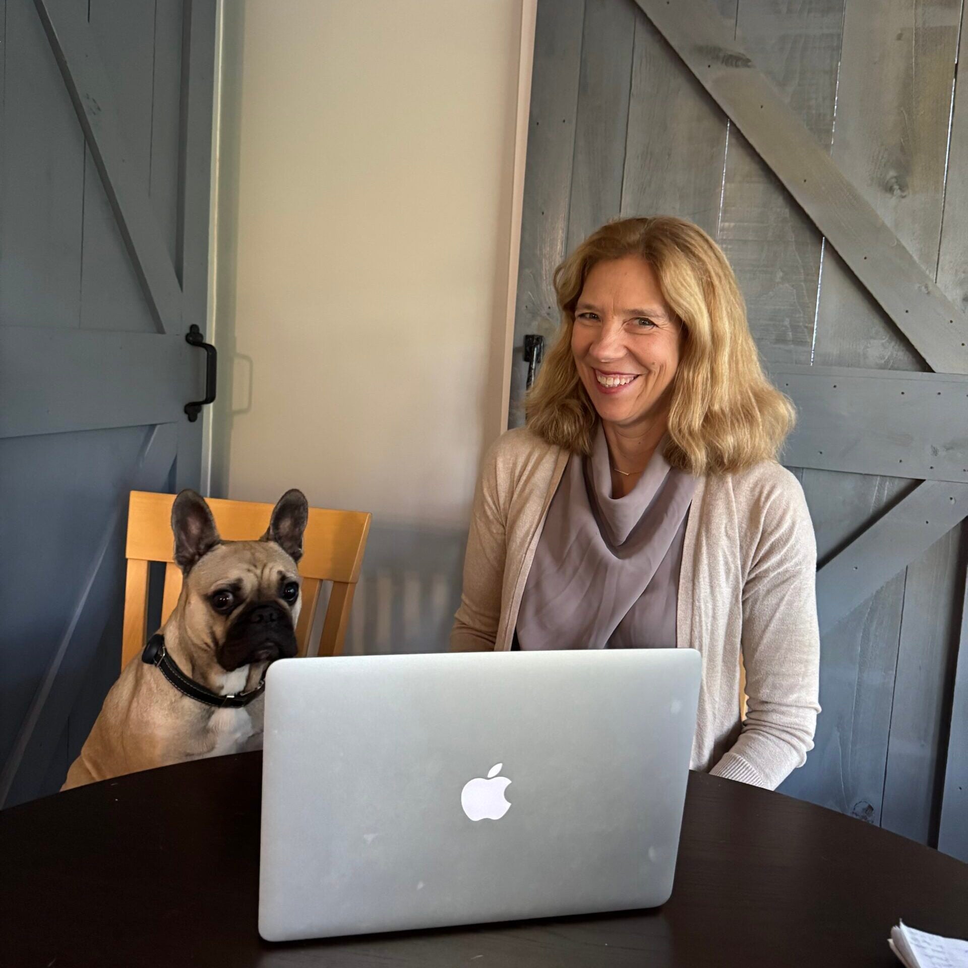 A Virtual Educator sitting behind her laptop and seated next to an attentive dog.