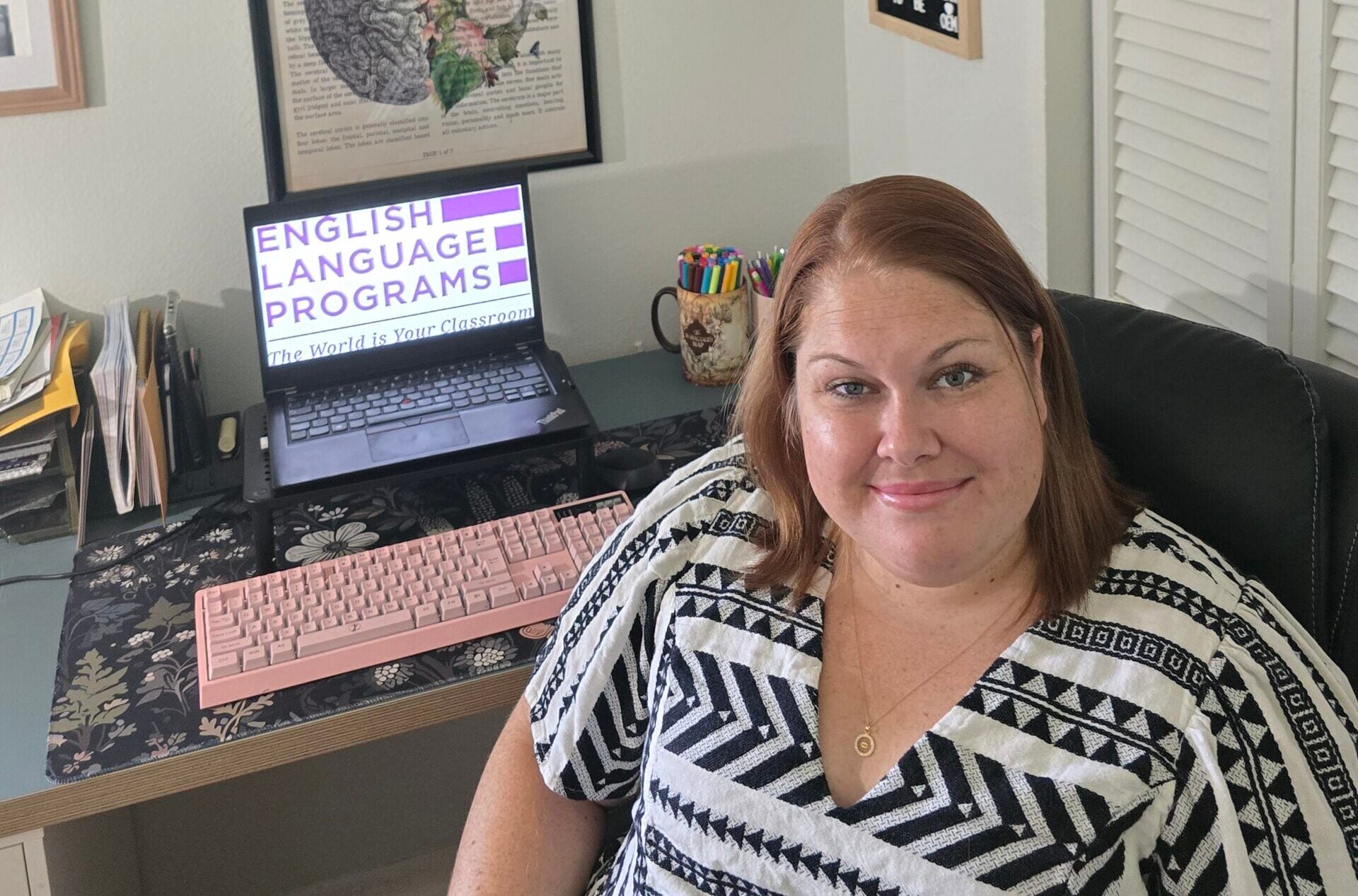 A Virtual Educator sitting at her desk with a laptop and facing the camera.