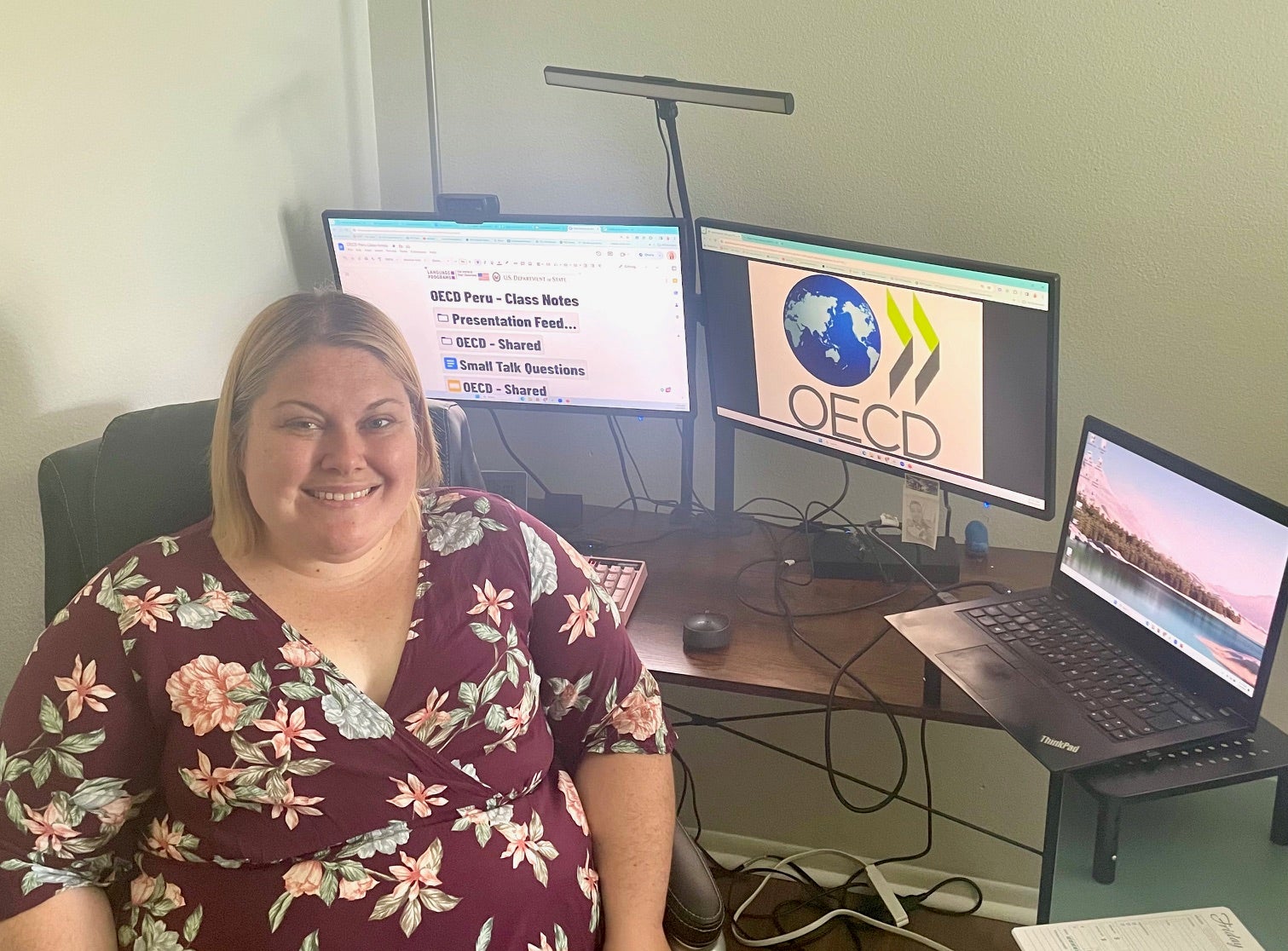 A Virtual Educator sits at her dual screen laptop workstation and faces the camera.